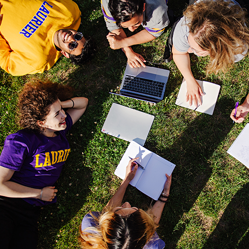 Students laying on the grass writing notes