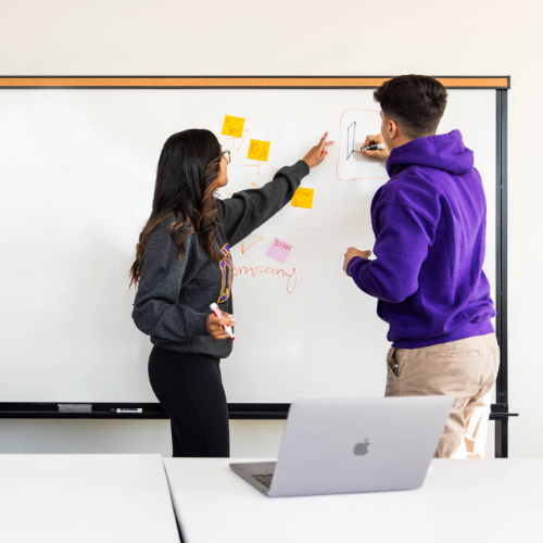 Two students writing on a white board