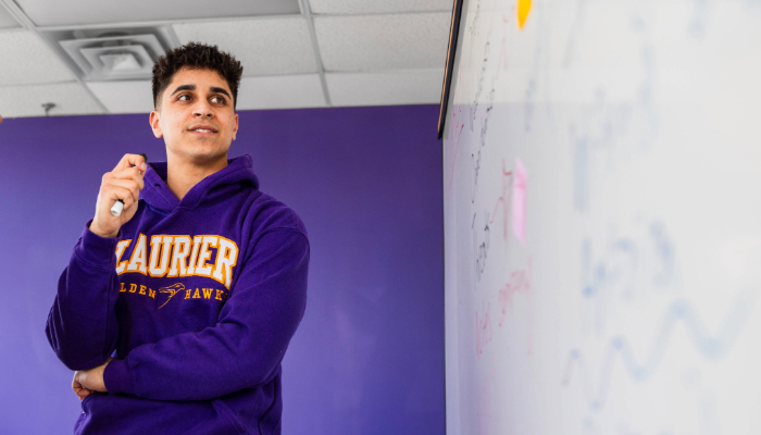 male student wearing purple laurier sweater in front of a white board
