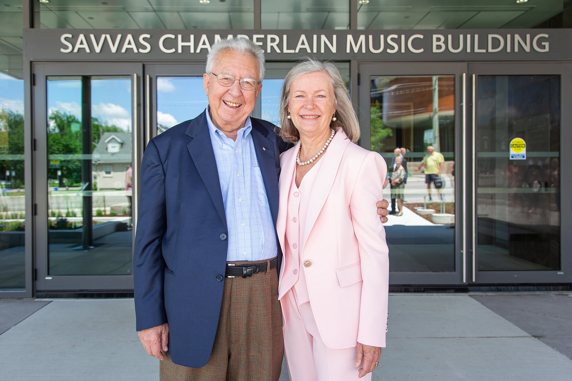 Savvas and Christine Chamberlain stand in front of doors with the name Savvas Chamberlain Music Building over them.