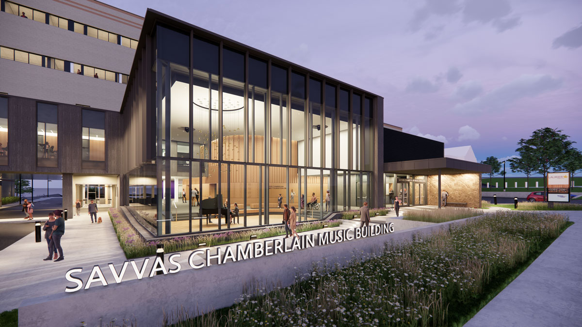 Front side close up view of the Savvas Chamberlain Music Building, with name sign at the bottom foreground, view into lobby through glass in the middle and entrance path to the left. Lobby looks bright and spacious. People are pictured throughout the image. 
