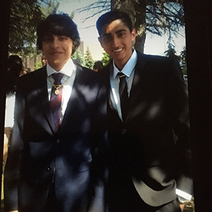 Nathan Eli John, right, stands under a tree with a friend. They are both wearing suits and smiling at the camera
