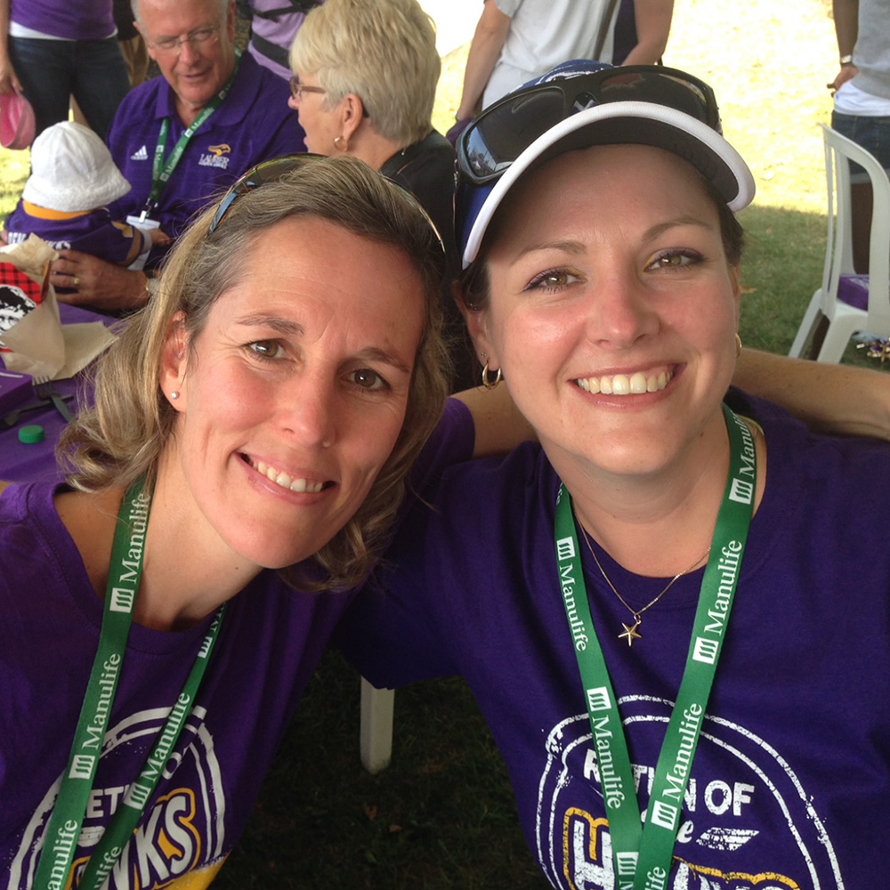 Julie and Leanne grin at the camera with their arms around each other. They are both wearing purple t-shirts saying 'Return of the Golden Hawks' on them.