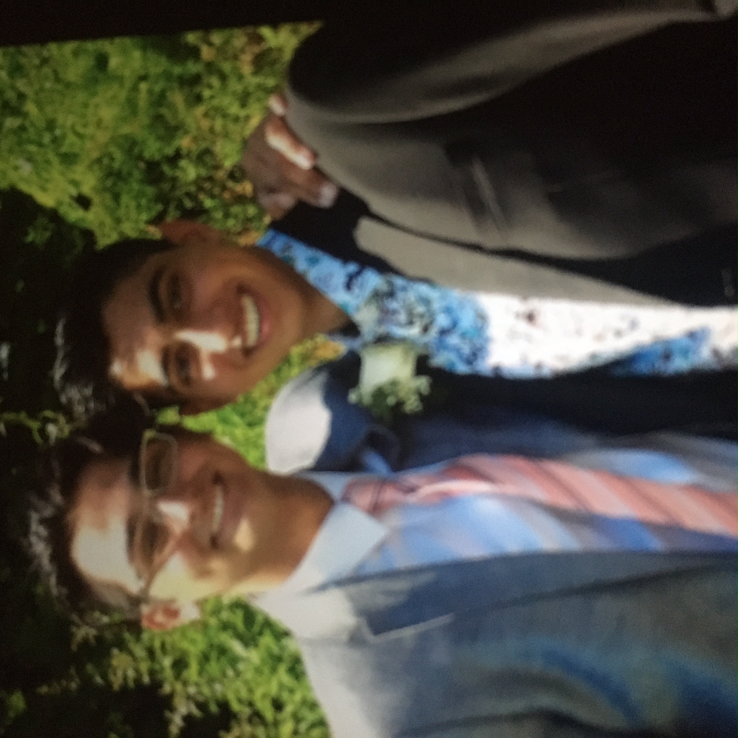 Nathan and a friend stand outside on a sunny day. They are wearing tuxedos with flower arrangements on their lapels.