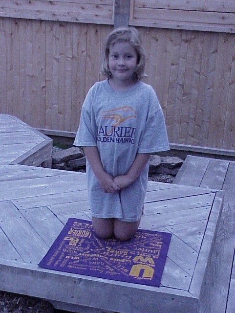 Olivia Saccucci as a child, wearing a large Laurier Golden Hawks t-shirt, kneeling on a Laurier hankerchief. 