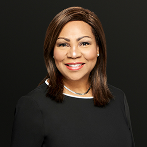 A professional portrait of a Black woman, Dr. Caroline Cole Power. She is dressed in black and smiles warmly at the camera.