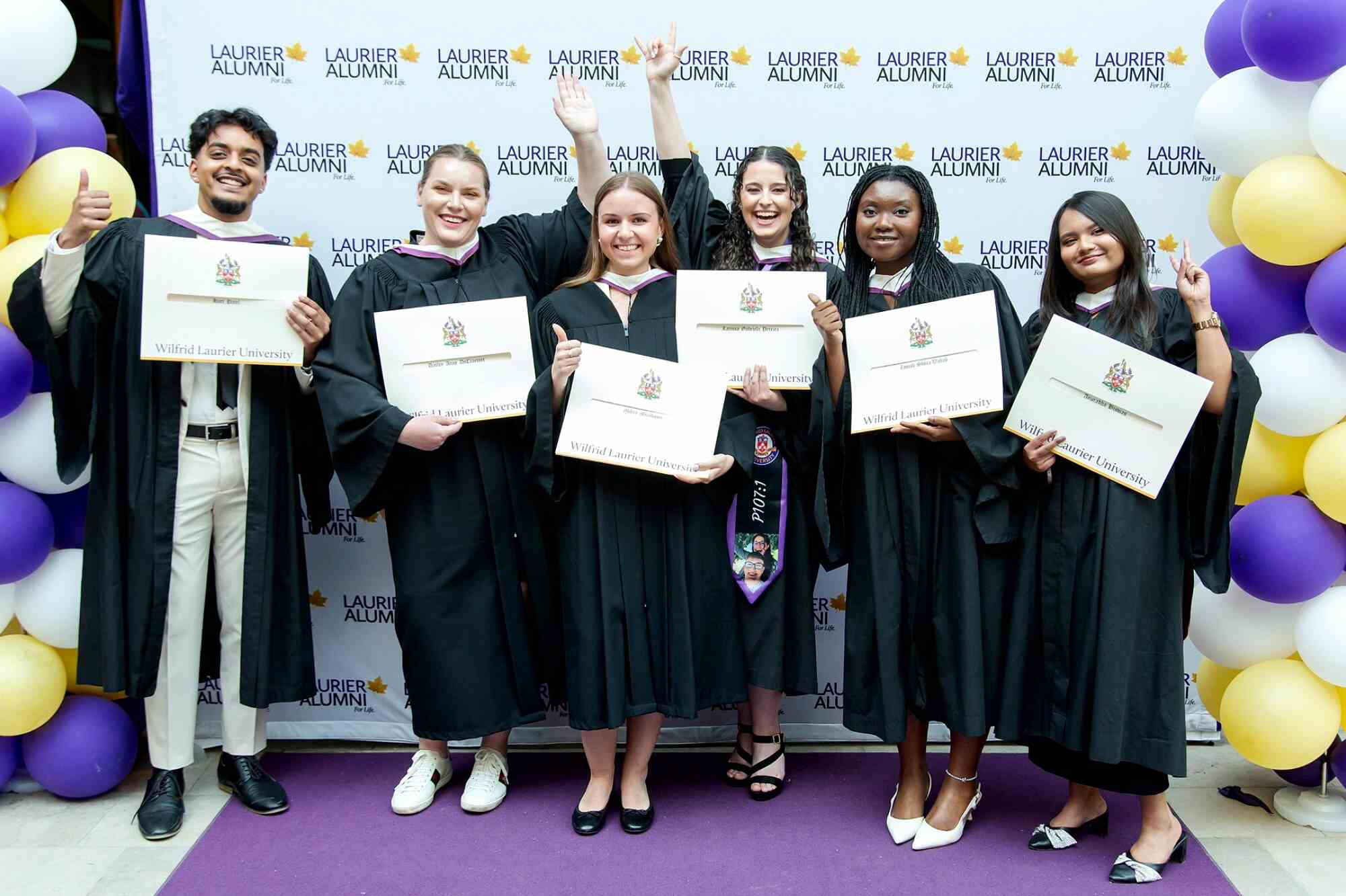 Group photo at spring 2025 convocation holding up their degrees in front of a 'Laurier Alumni' banner