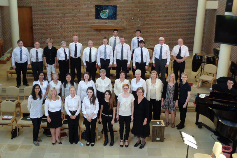 A choir of about 30 young and older people wearing black and white, posed at the front of a church, photographed from above.