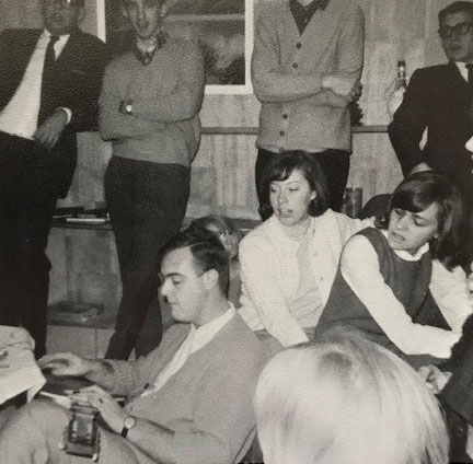 Students at a party watch a young man play guitar.