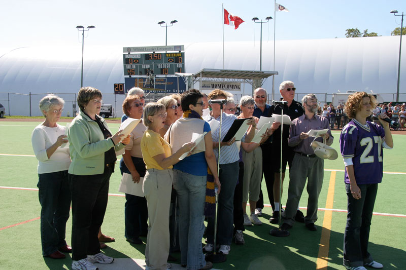 A group of about 15 people singing on a football field.